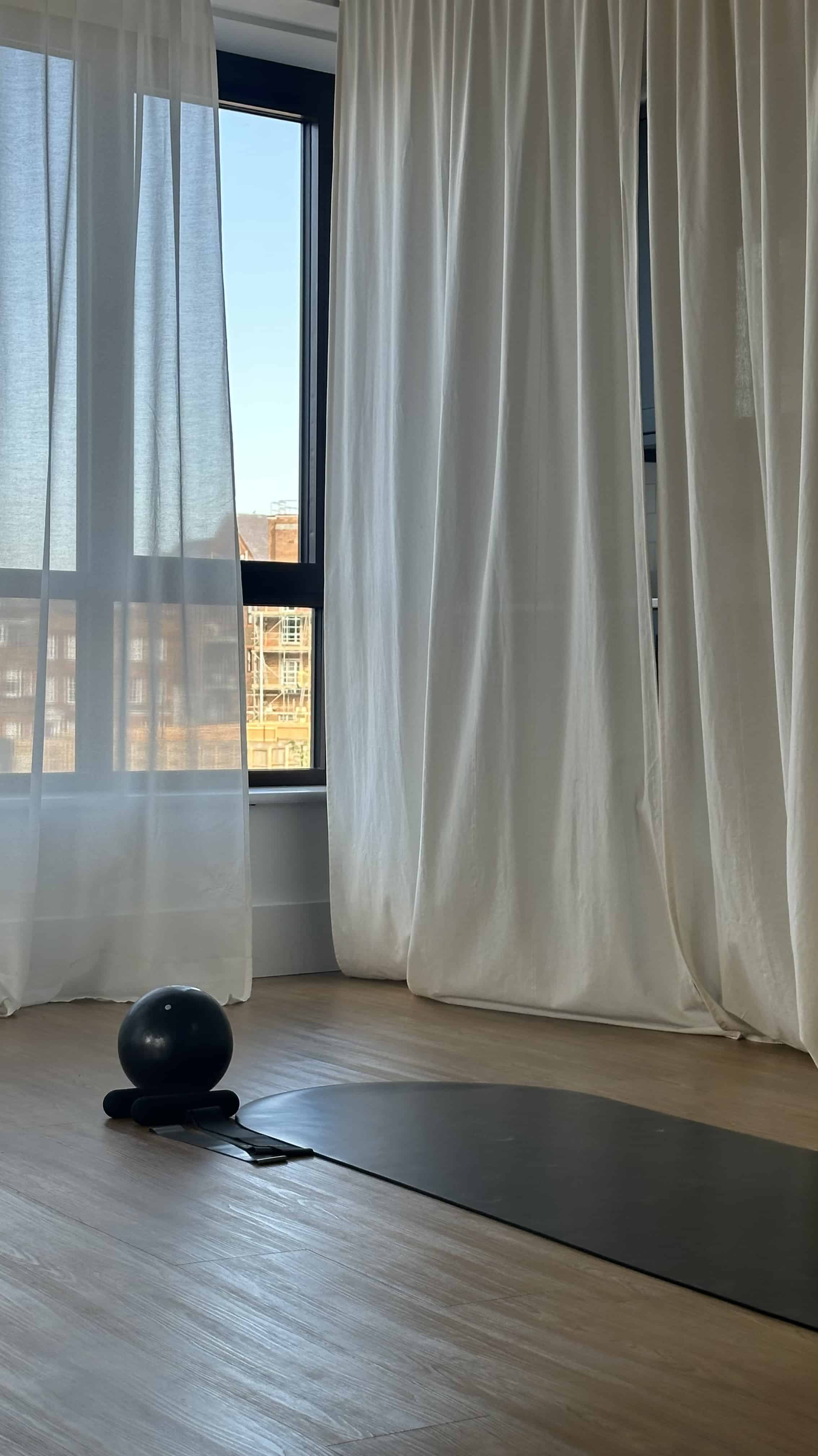 fitness studio with window, white curtains, exercise mat and exercise ball