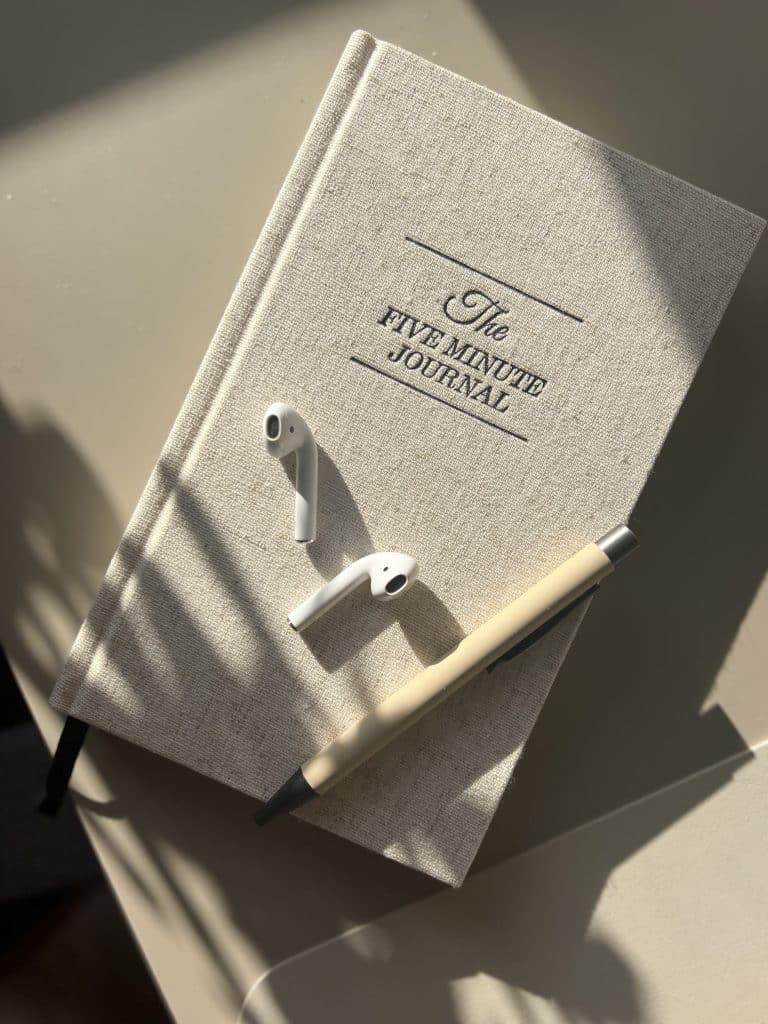 the five minute journal sitting on desk with airpods and pens