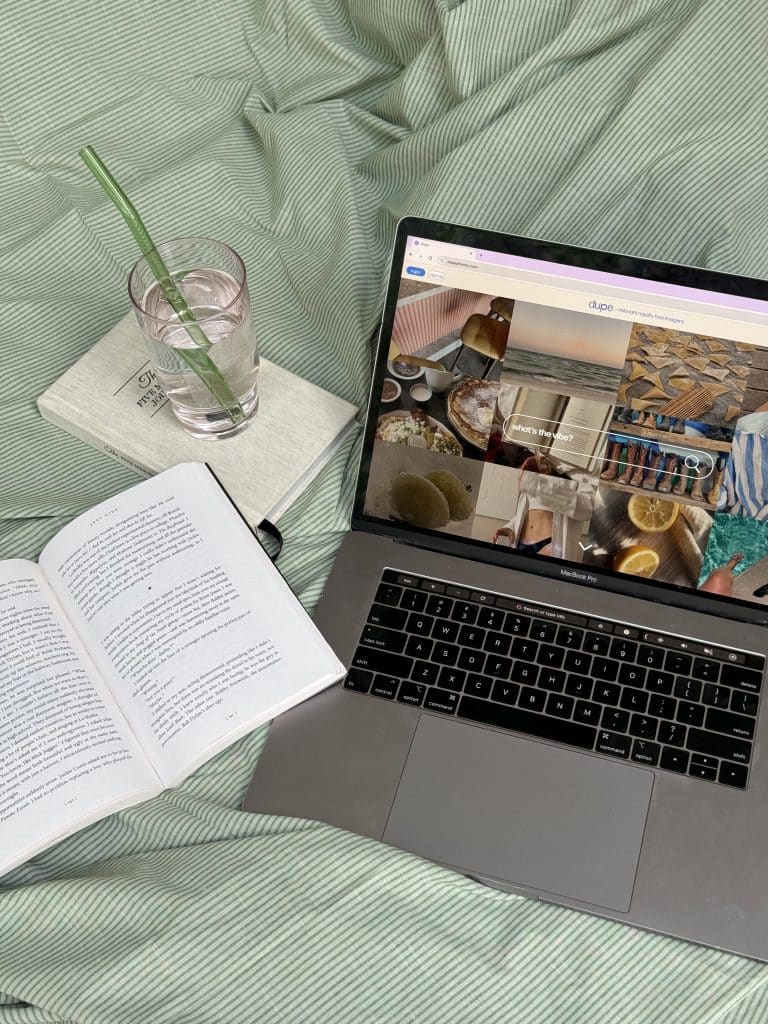 computer, book, and glass of water sitting on a bed