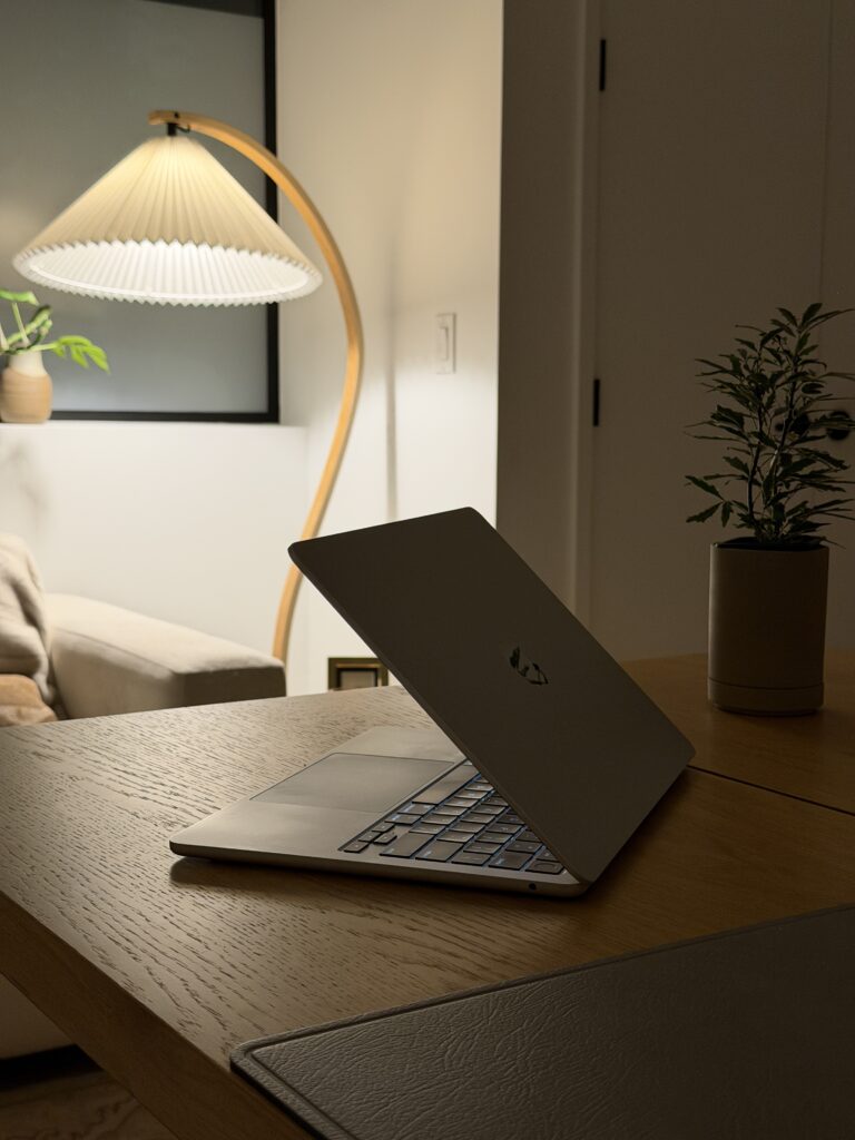 computer sitting on a desk in a living room with a lamp in the background