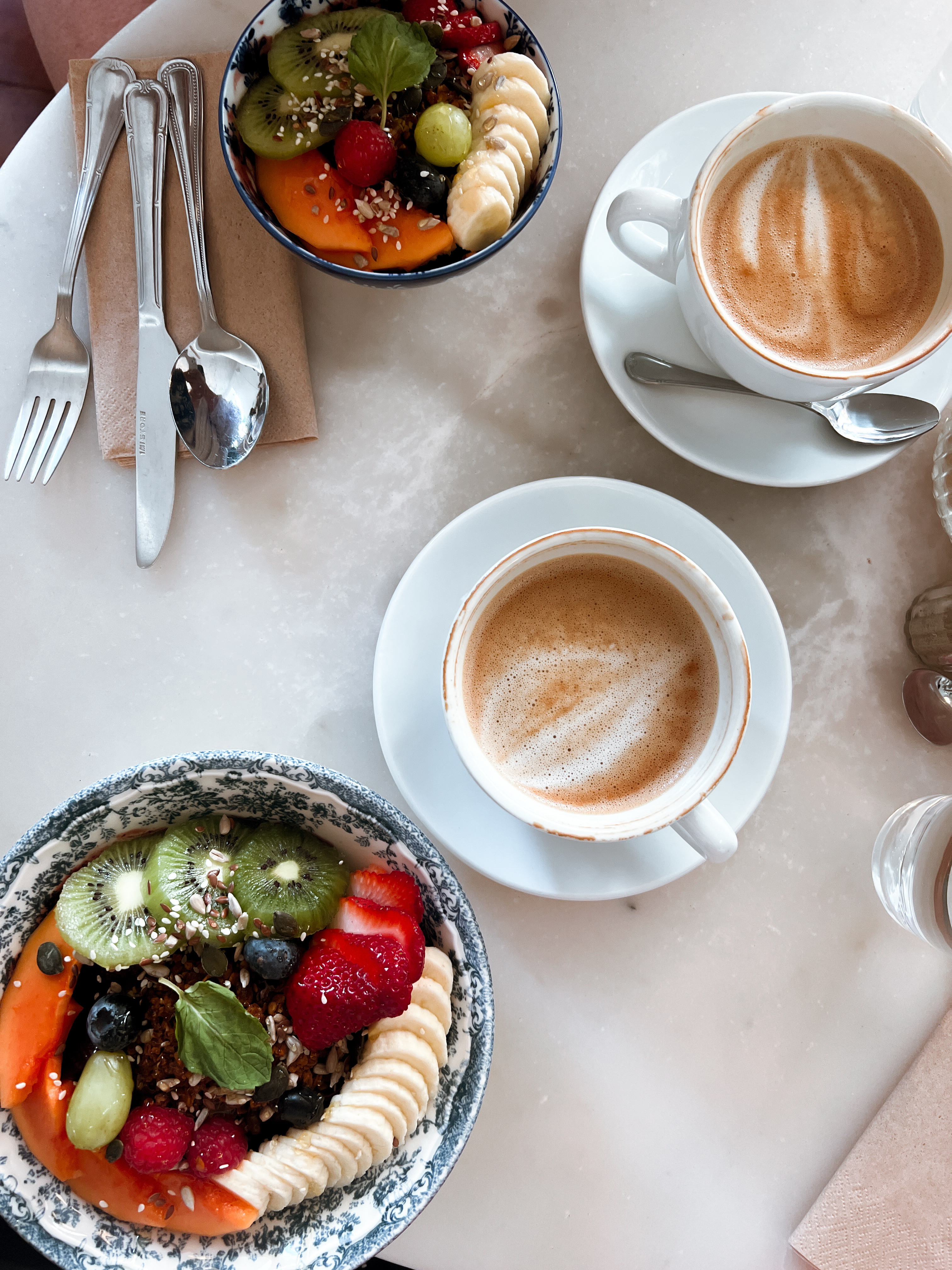 two lattes and two bowls of fruit sitting on a table