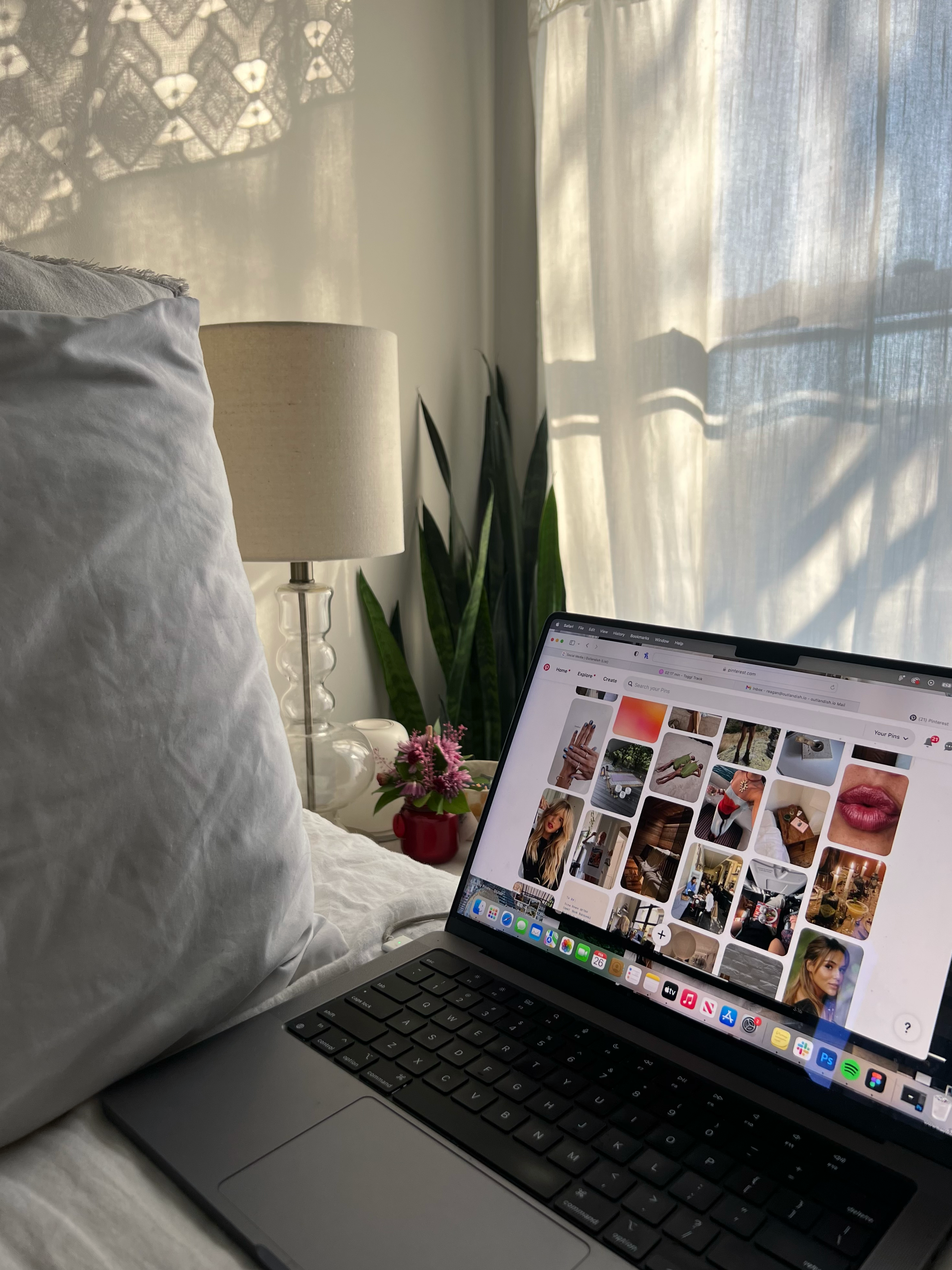 Laptop on white bed sheets in bright room, screen showing website design for therapists on Pinterest, with lamp, plant, mug, and sheer curtains