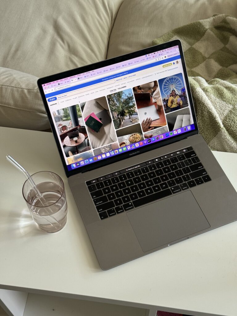 Laptop displaying on-page SEO for therapist pins next to a straw-filled water glass on a desk beside beige couch with plaid blanket