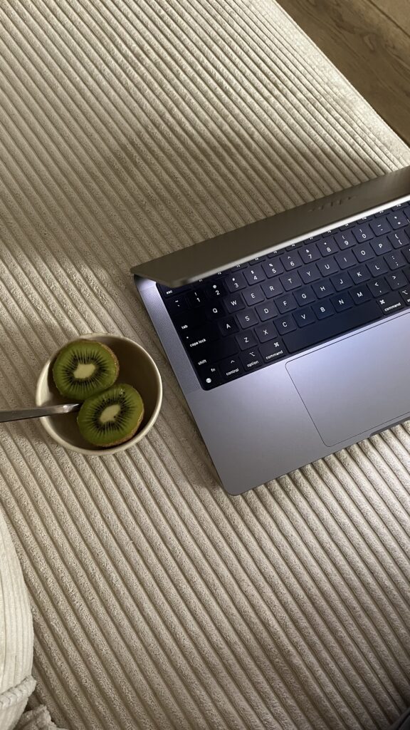 A laptop rests on a textured couch next to a bowl of sliced kiwis, a perfect setting for creating content on seo for dietitians