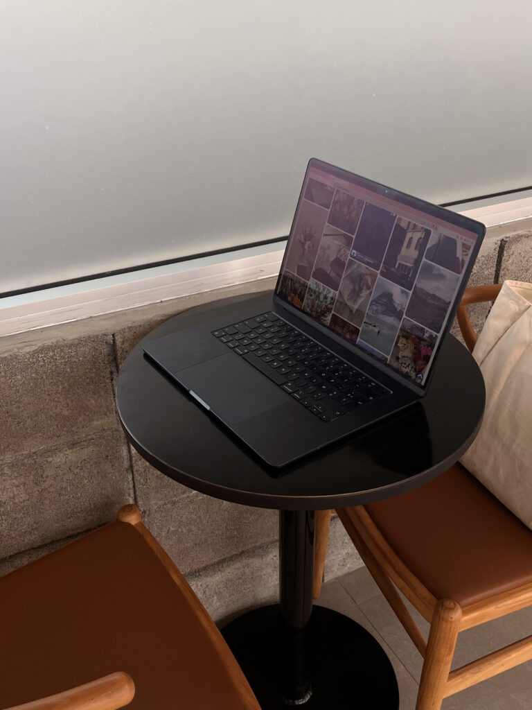 A modern laptop rests on a small round table with two chairs, showing a layout like a professional therapist website.