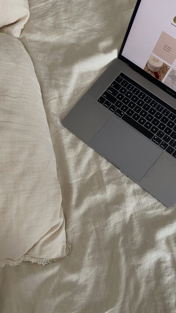 Gray laptop resting on a beige bedspread, keyboard visible, screen showing a grid of images/pages