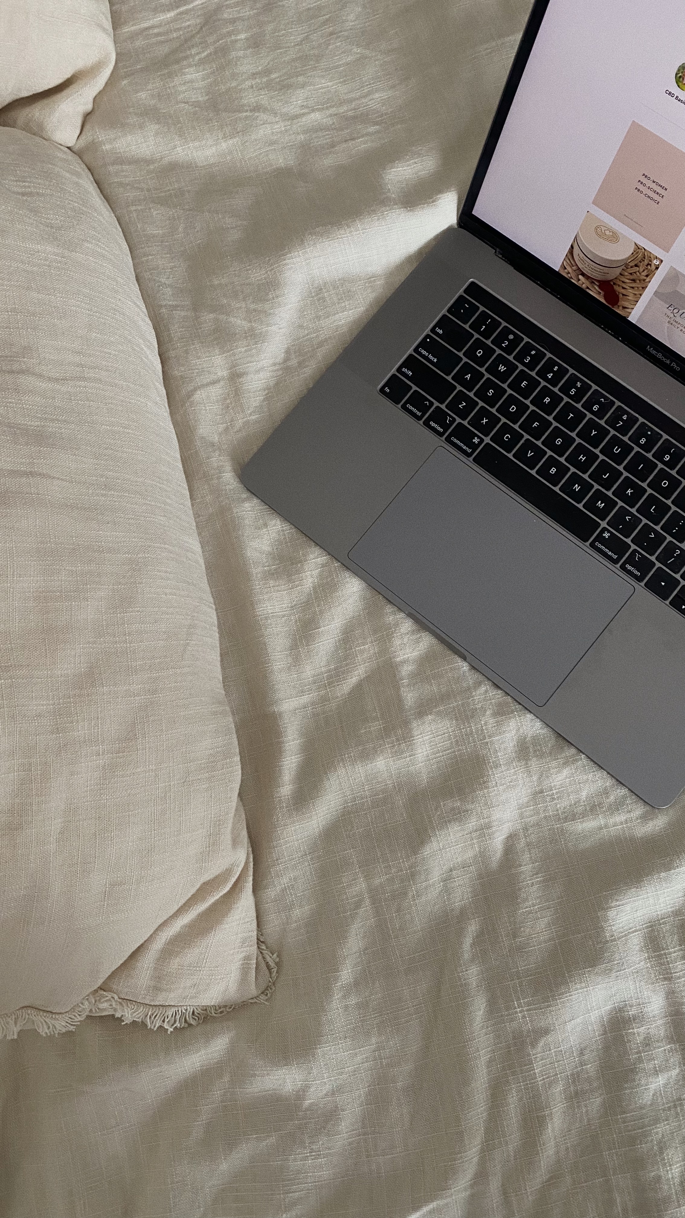 Gray laptop resting on a beige bedspread, keyboard visible, screen showing a grid of images/pages