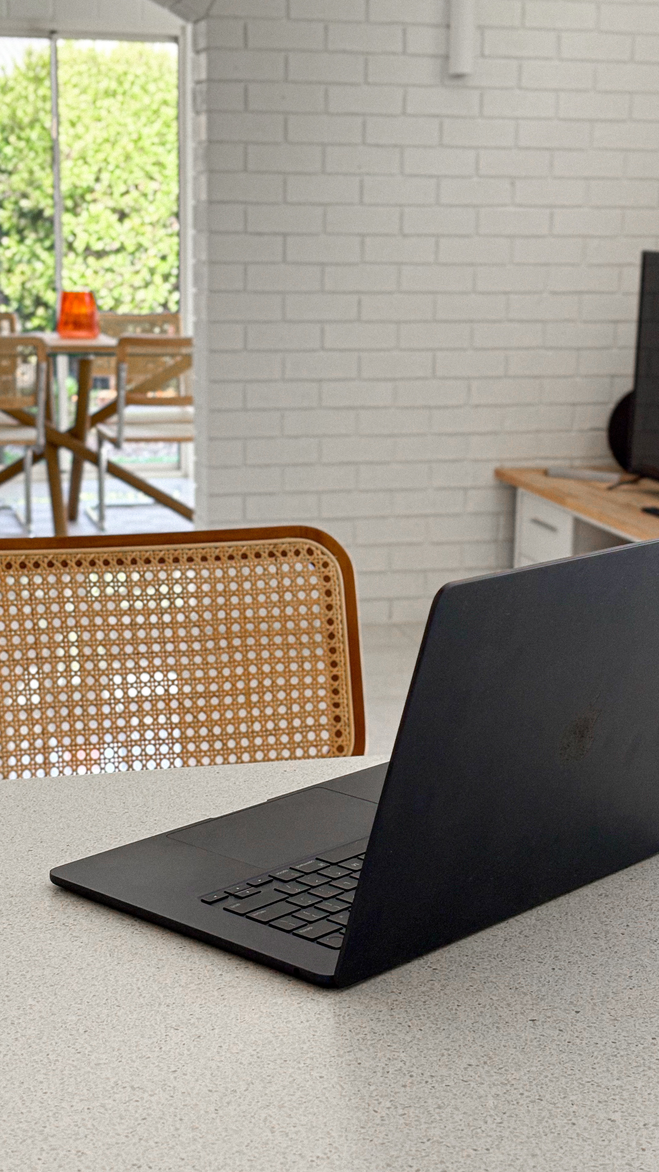 Open black laptop on a light desk in a bright room with a rattan chair, highlighting website features.