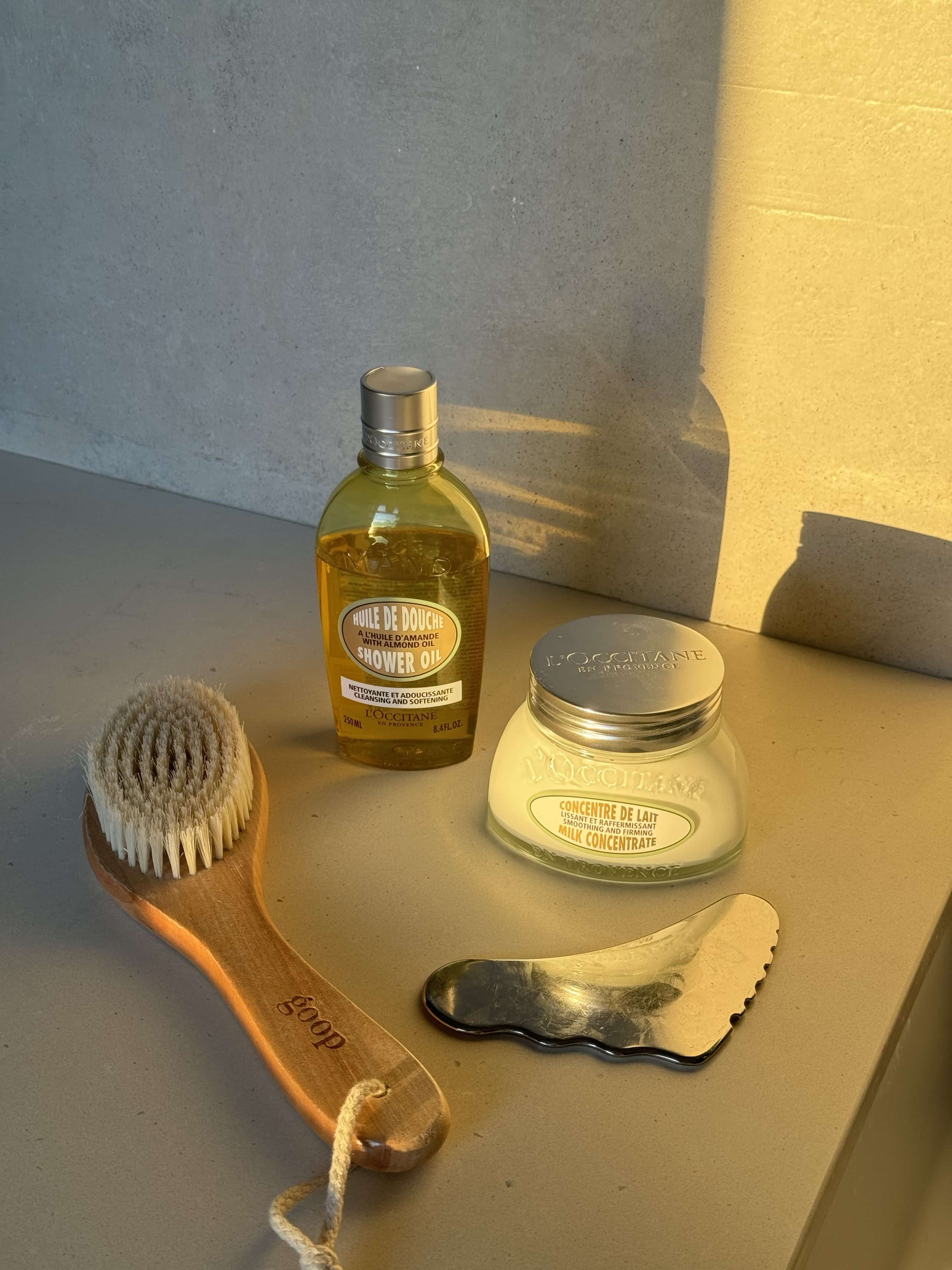 Dry brush, gua sha, shower oil, and body lotion on a counter for National Self Care Awareness Month