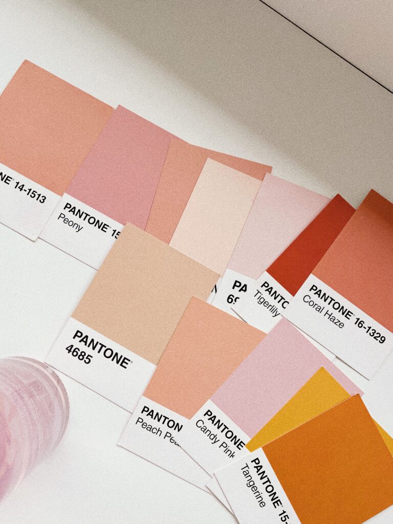 Peach, pink, orange, and yellow Pantone swatches arranged on a white desk for branding questions.