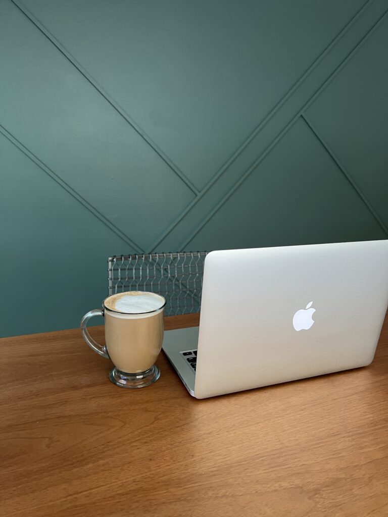 Laptop and coffee mug on a wooden table with a green geometric wall, suggesting a web design workspace